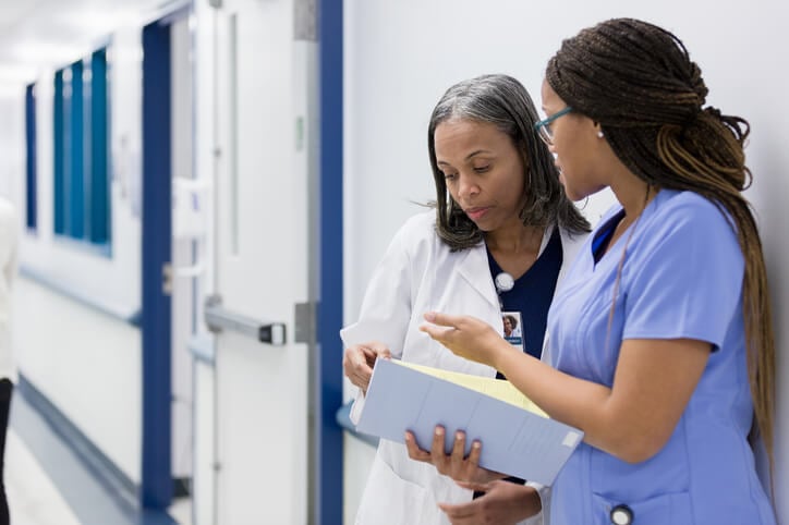 nurse and doctor discussing file in hospital hallway