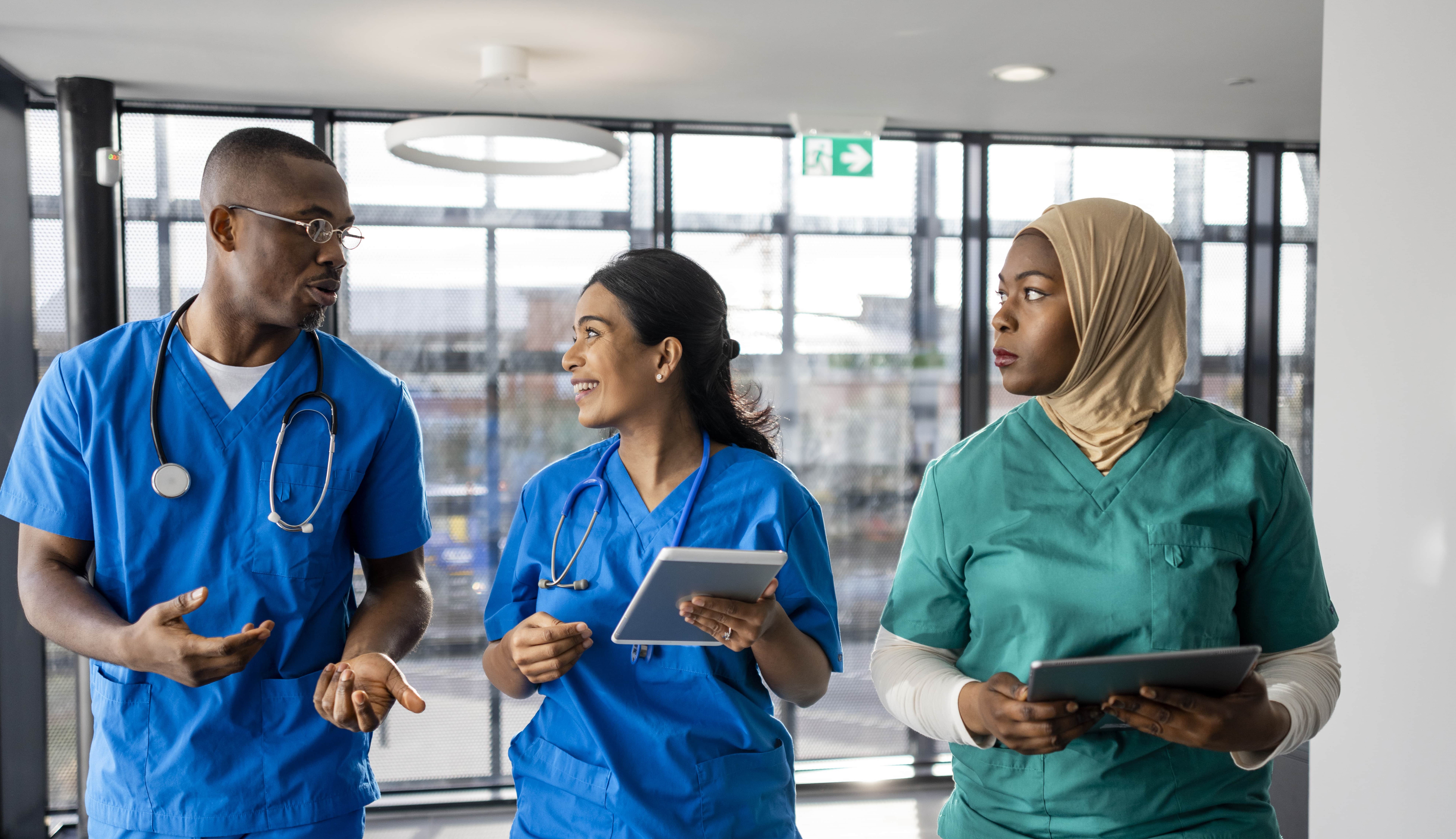 Three clinicians conversing in a healthcare facility hallway