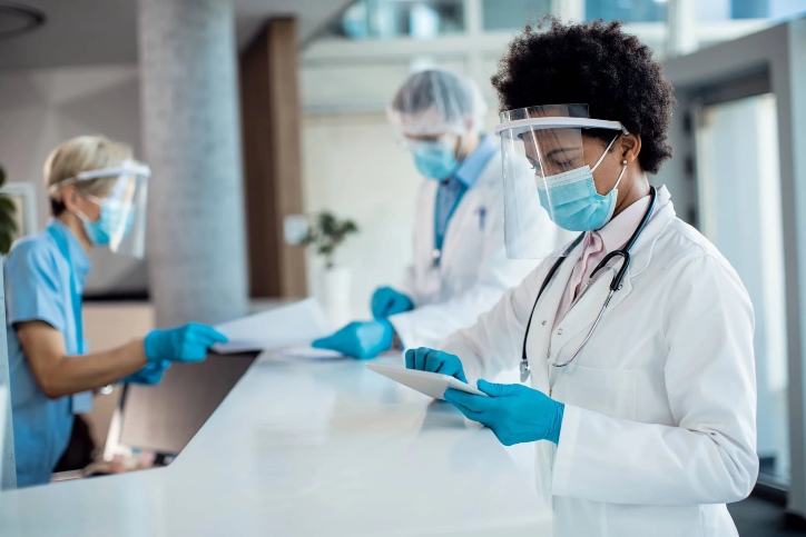 A masked and gloved doctor focused on a tablet