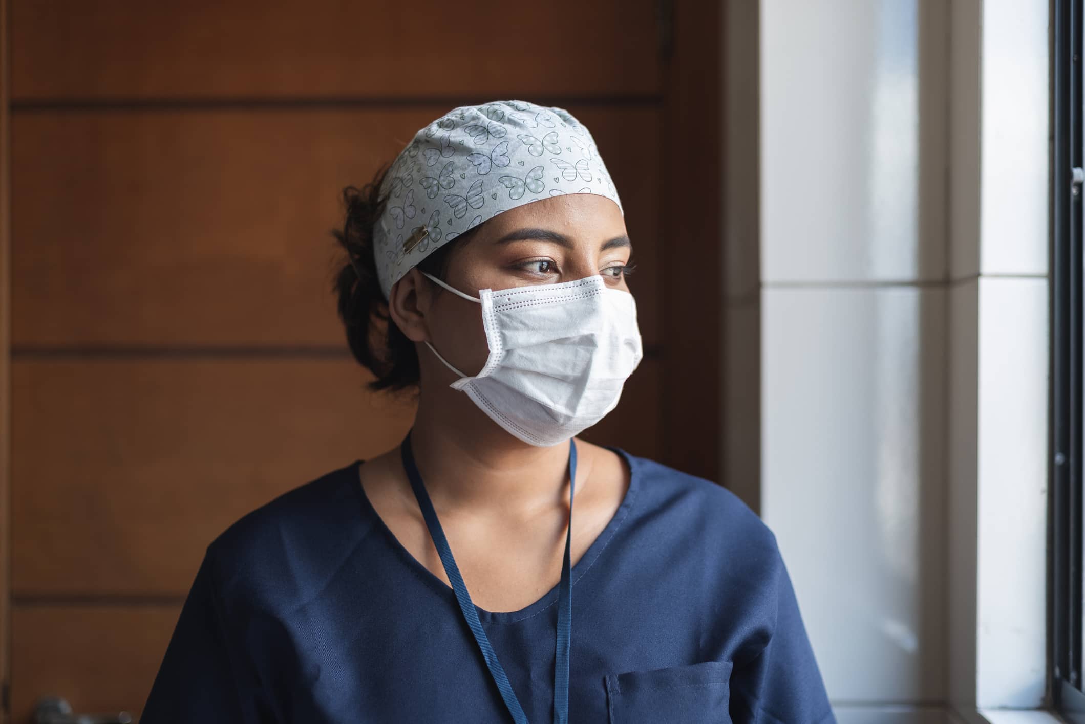 Travel nurse in scrubs and mask gazing out the window Travel nurse in scrubs and mask gazing out the window