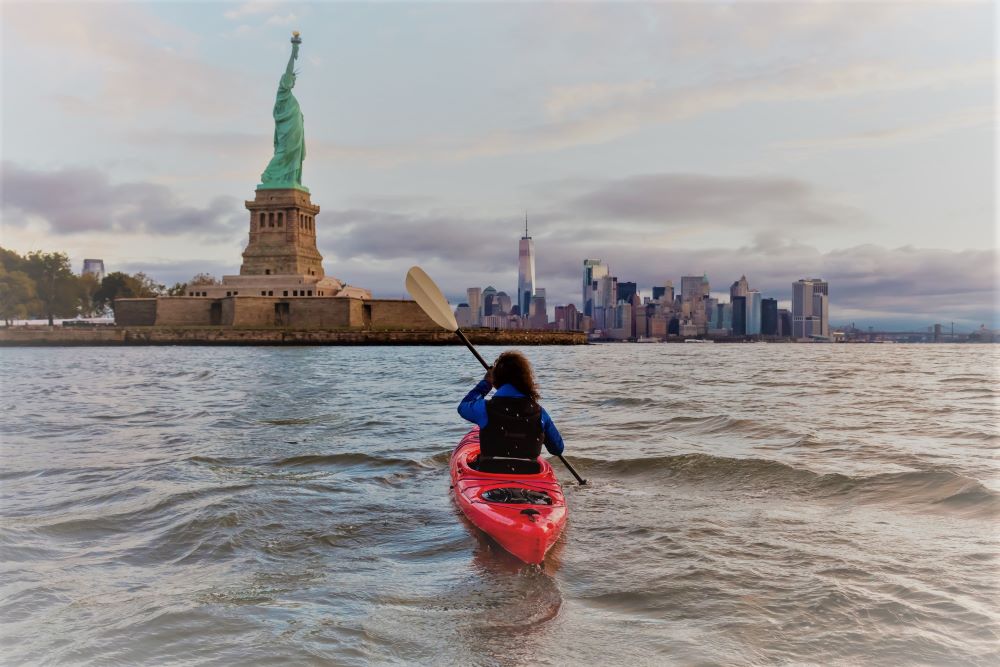 person in red vest kayaking across the river